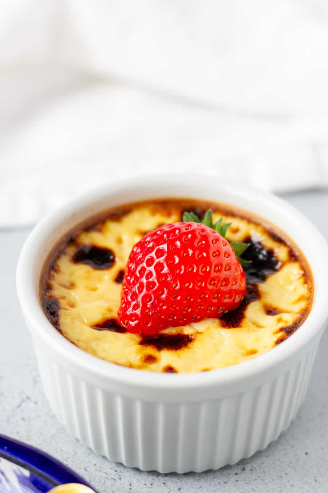 Single custard in a white ramekin with a strawberry on top.