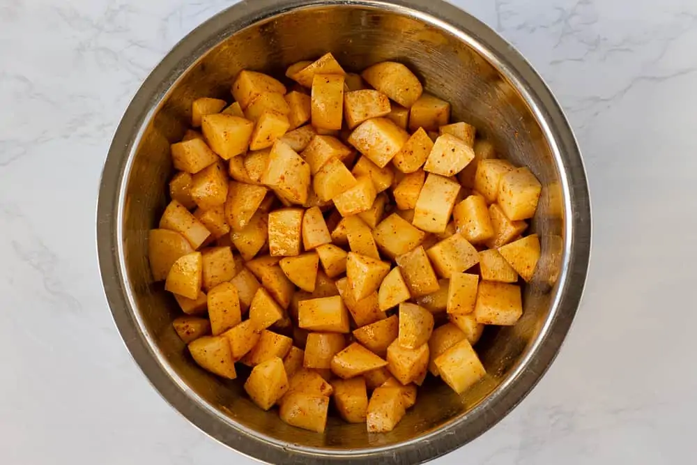 Diced potatoes in a silver bowl with seasoning.