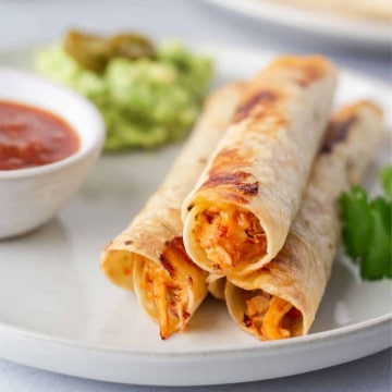 Up close view of salsa chicken flautas on a plate with a side of salsa.