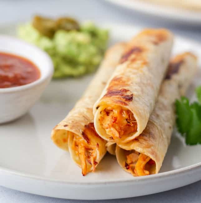 Up close view of salsa chicken flautas on a plate with a side of salsa.