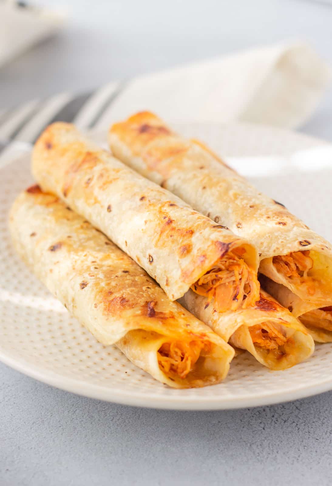 Plate of chicken rolled tacos stacked together.