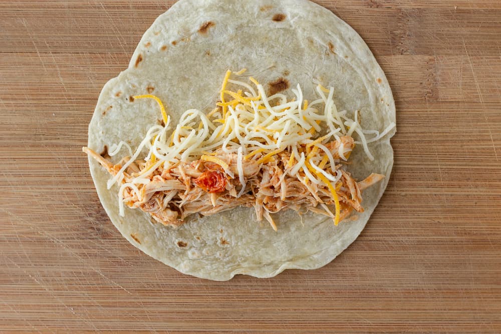 Tortilla on a cutting board with shredded chicken and cheese in the middle.