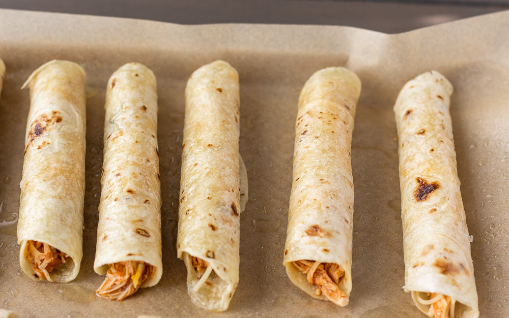 Rolled Flautas on a baking sheet with parchment paper, ready to go in the oven.