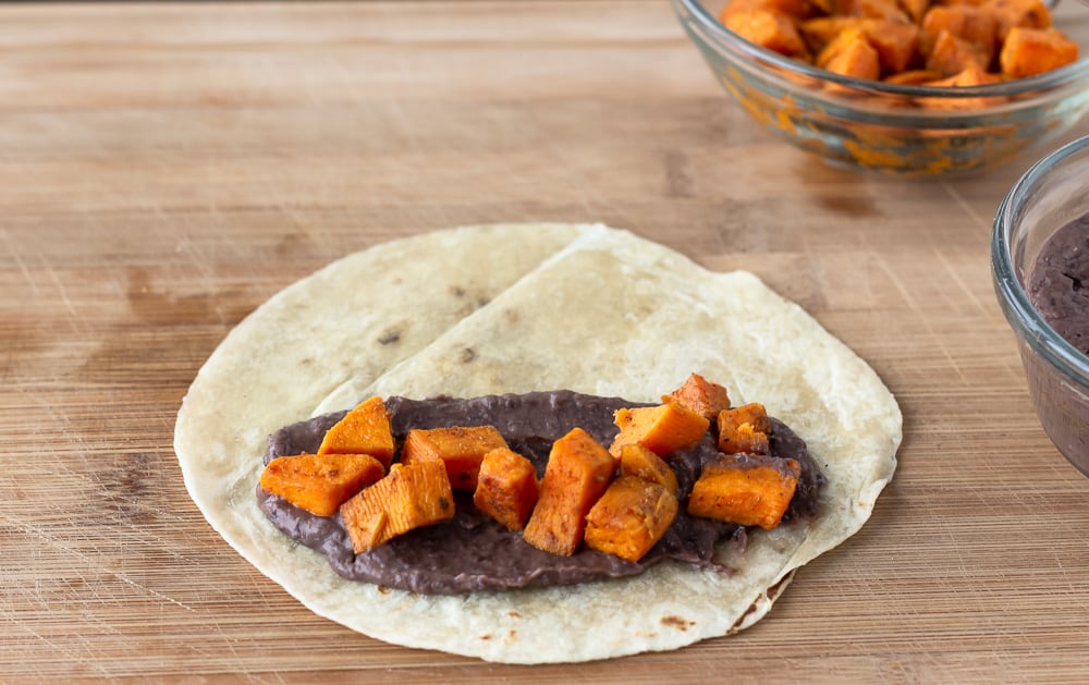 Flour Tortilla on a cutting board layered with black beans and sweet potato.