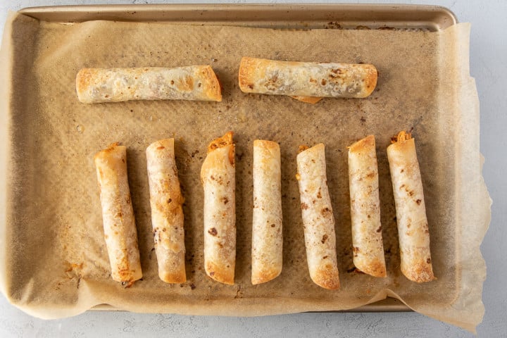 Baked flautas out of the oven on a baking sheet lined with parchment paper.