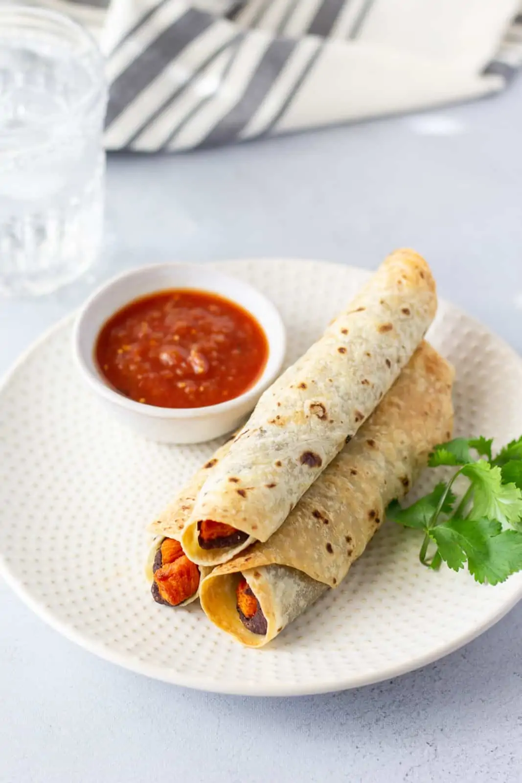 3 sweet potato flautas on a plate with a side of salsa and cilantro garnish.