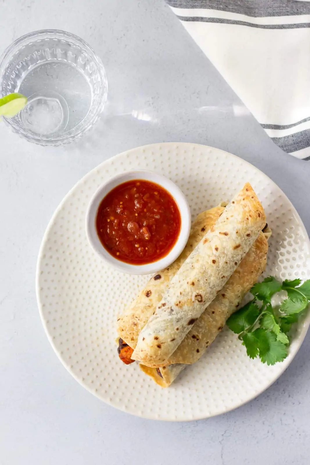 Overhead view of 3 flautas on a plate with a side of salsa and a glass of water on the side.