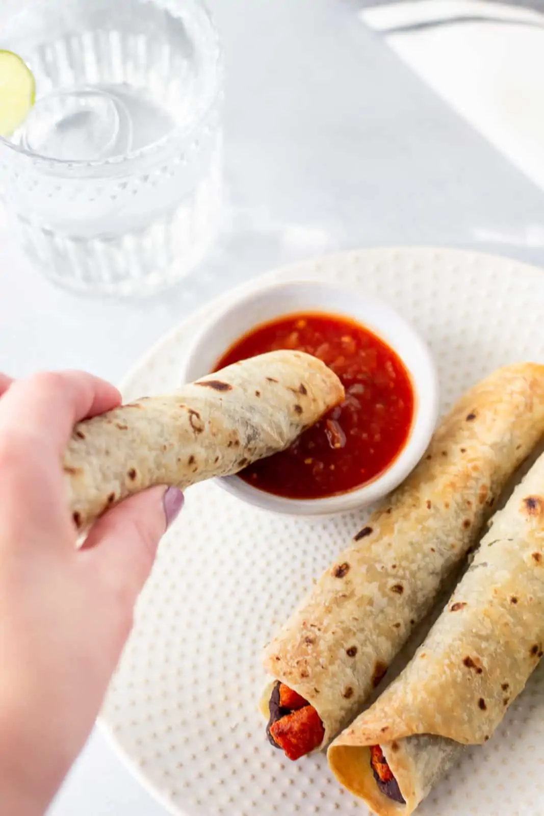 Hand holding a rolled taco that's being dipped into a small bowl of salsa.