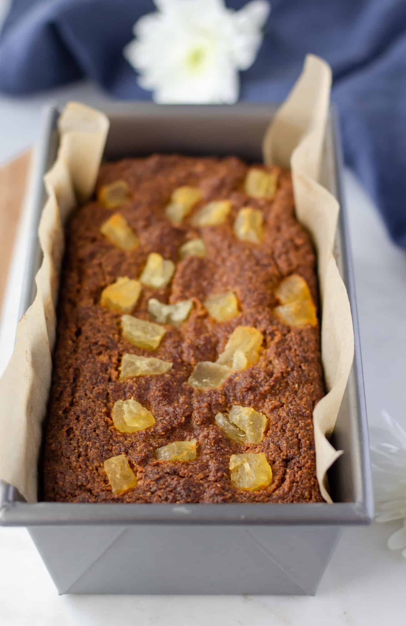 Baked loaf in the pan with parchment paper and dried pineapple on top.