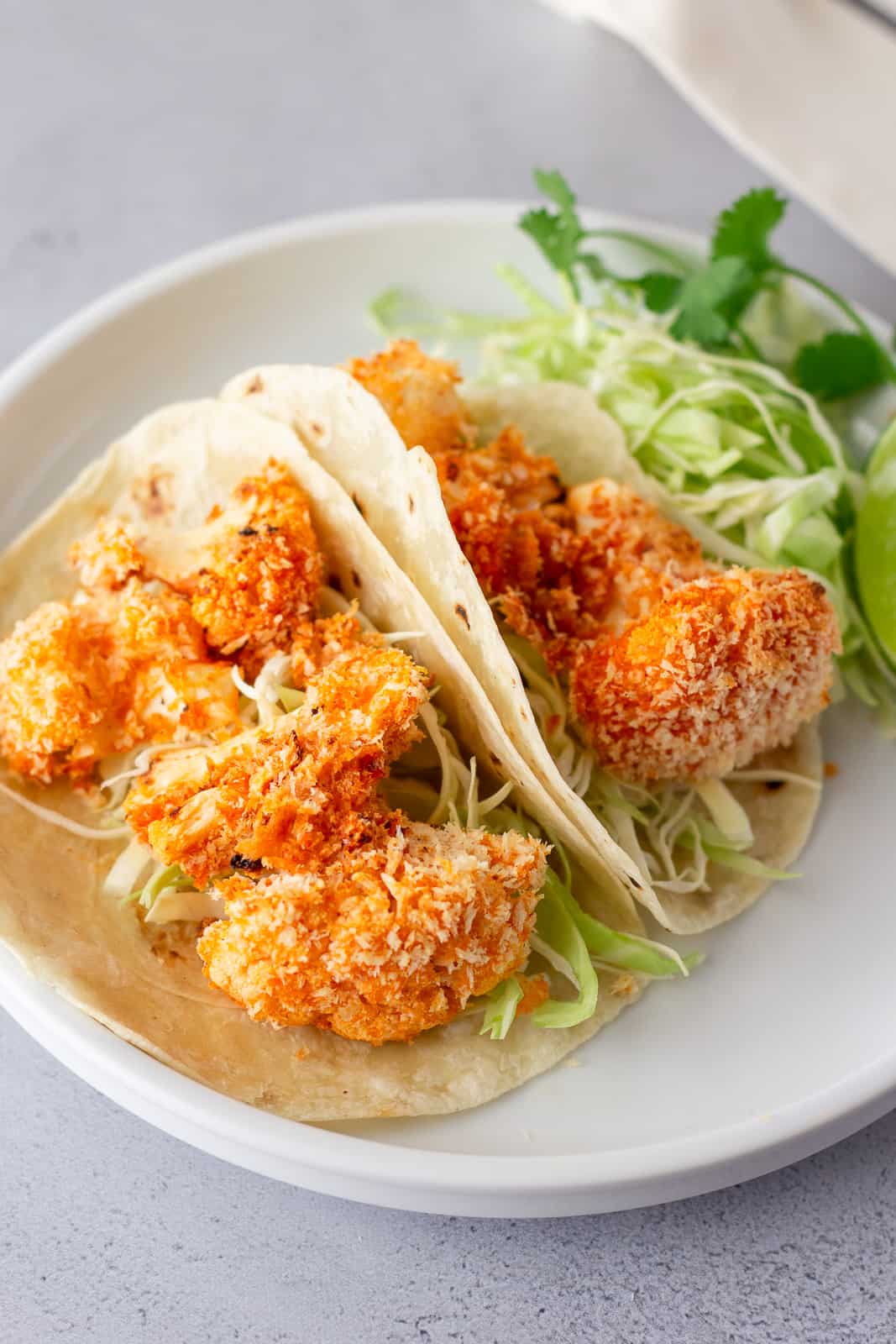 white plate with tortillas, shredded lettuce and panko buffalo cauliflower.