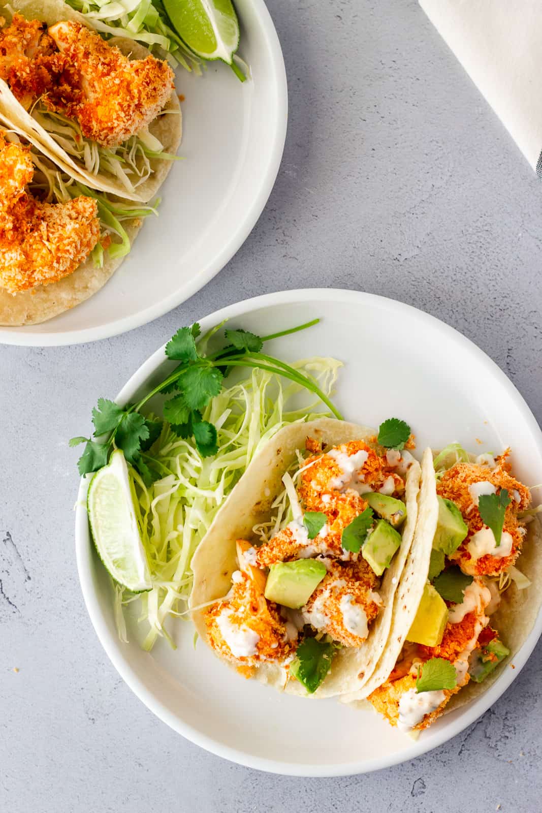 Overhead view of buffalo cauliflower tacos on a white plate with shredded lettuce, cilantro, and lime on the side.