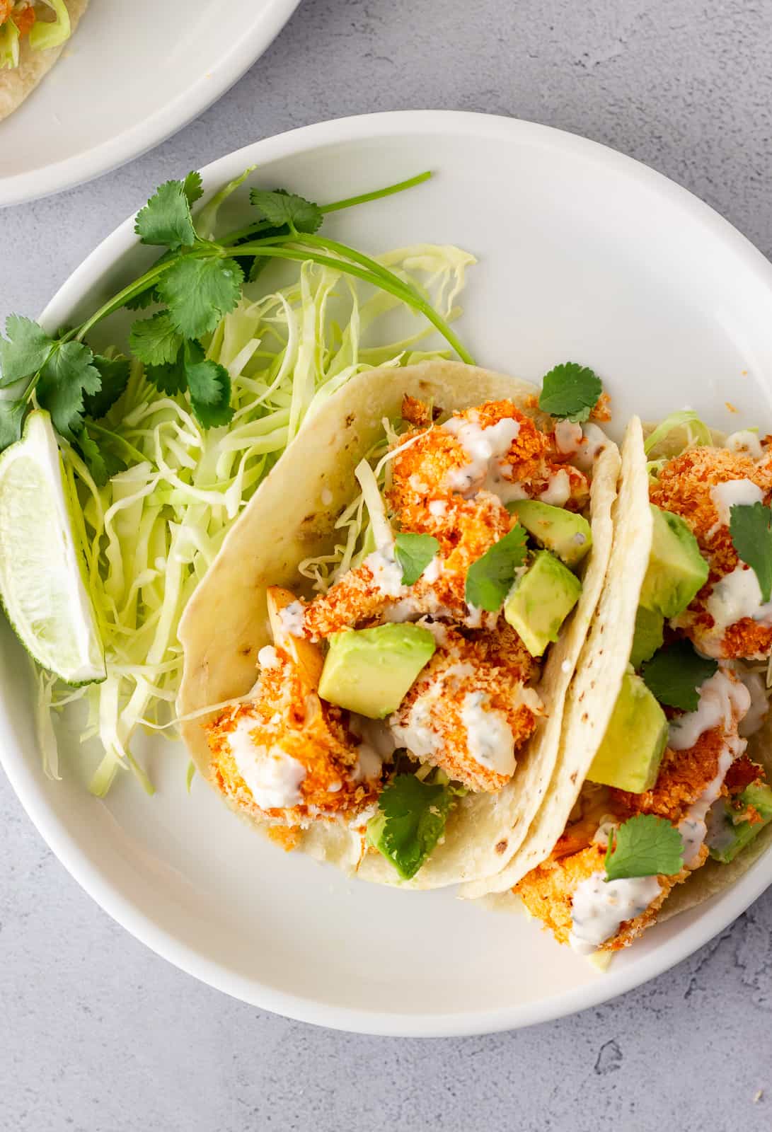 Overhead view of tacos on a white plate topped with ranch and diced avocado.