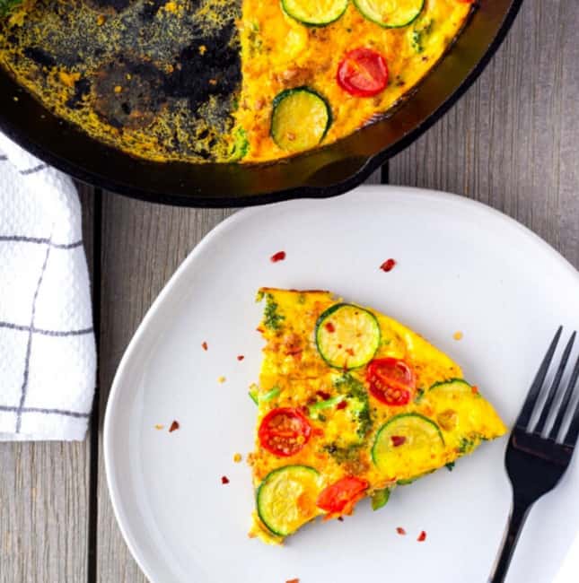 Slice of frittata on a plate with a large skillet on the side.