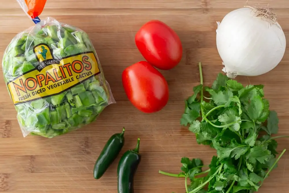 Ingredients on a cutting board, Nopalitos, roma tomatoes, white onion, cilantro, and jalapeno.