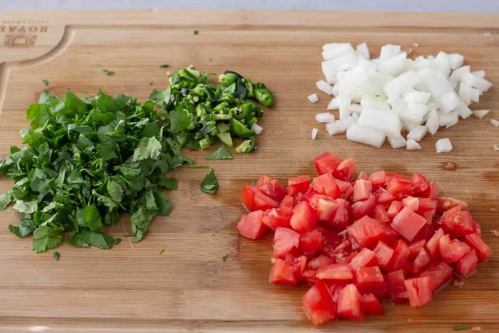 Cutting board with chopped tomato, onion, cilantro, and jalapeno.