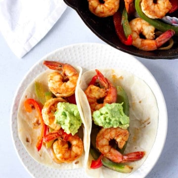 Two Shrimp Fajita tacos on Flour tortilla and a skillet of more shrimp on the side.