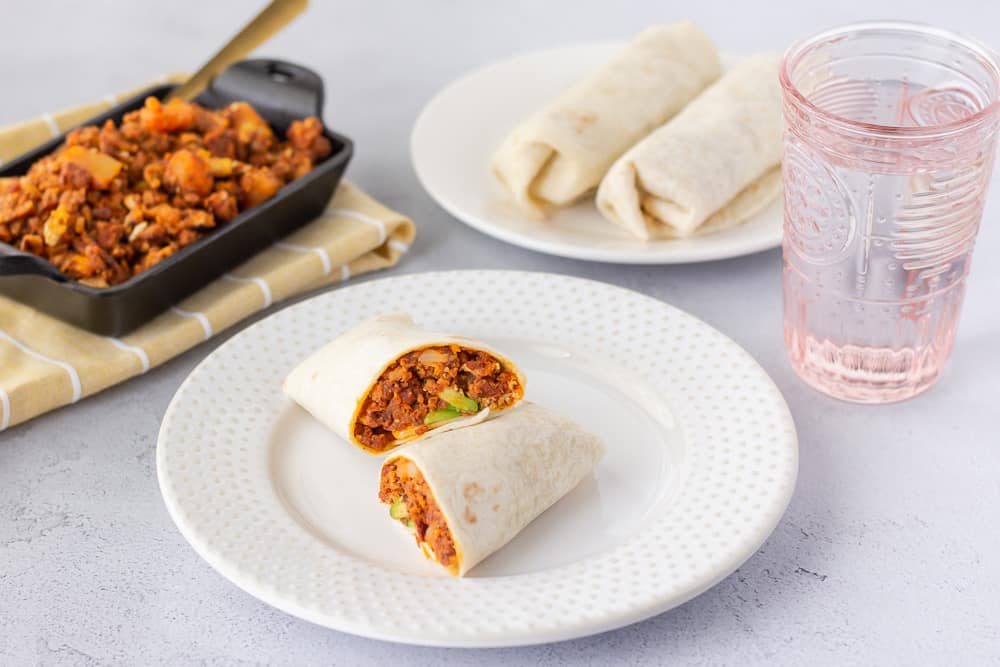 Horizontal view of burrito on a plate and a pink glass of water on the side.