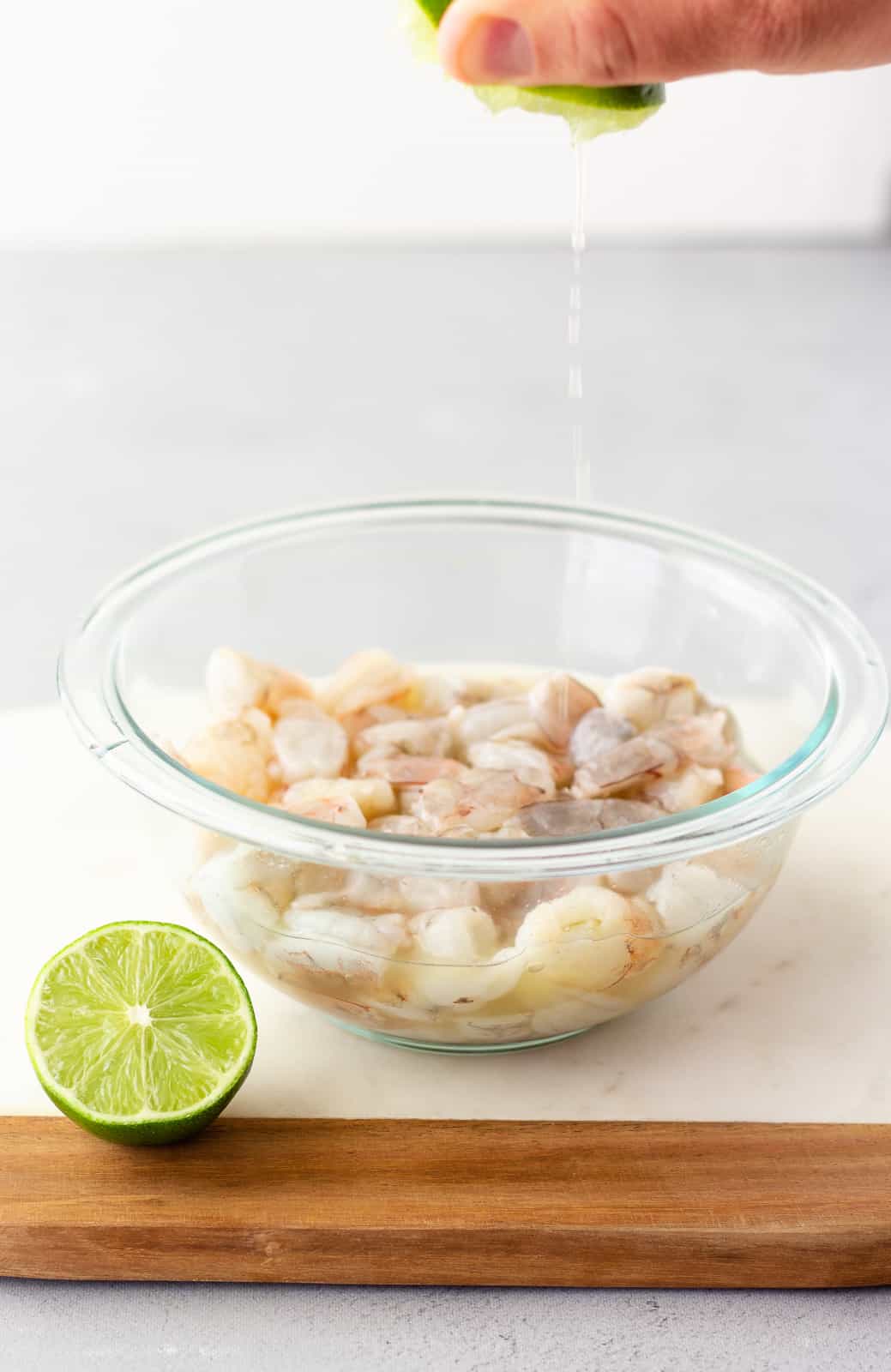 Glass bowl with raw shrimp and lime being squeezed into the bowl.