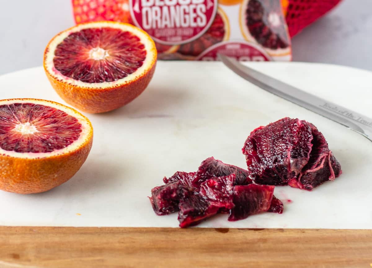 Diced blood orange and one cut in half on a marble cutting board.