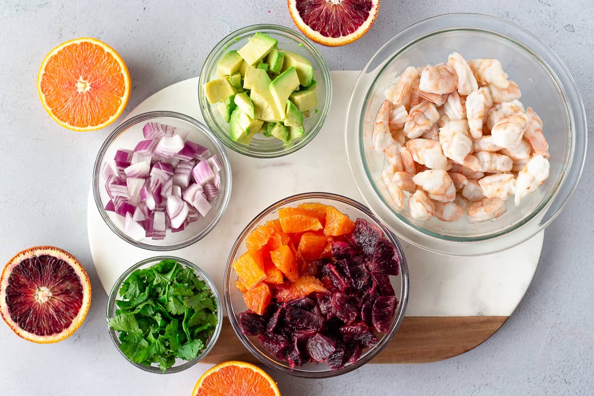 Ingredients for citrus ceviche- shrimp, diced avocado, red onion, cilantro, sliced oranges around the ingredients.