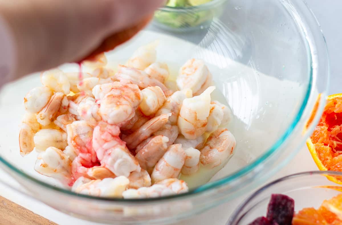 Glass bowl with shrimp and hand squeezing an orange into the bowl of shrimp.