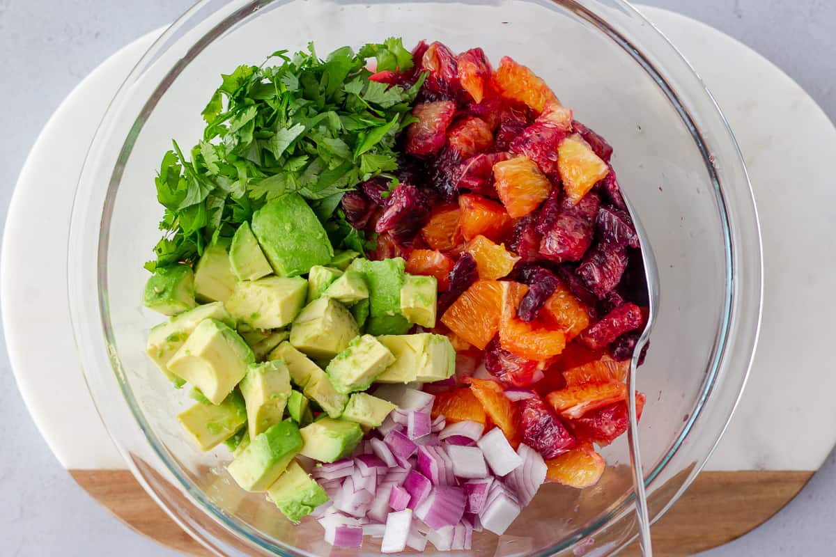 Glass bowl with diced blood oranges, oranges, red onion, avocado, and cilantro.