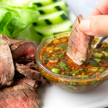 Hand holding a piece of steak being dipped into a spicy sauce.