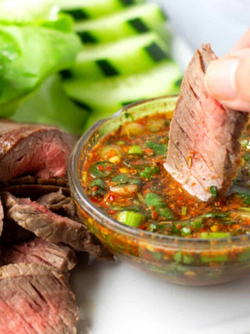 Hand holding a piece of steak being dipped into a spicy sauce.