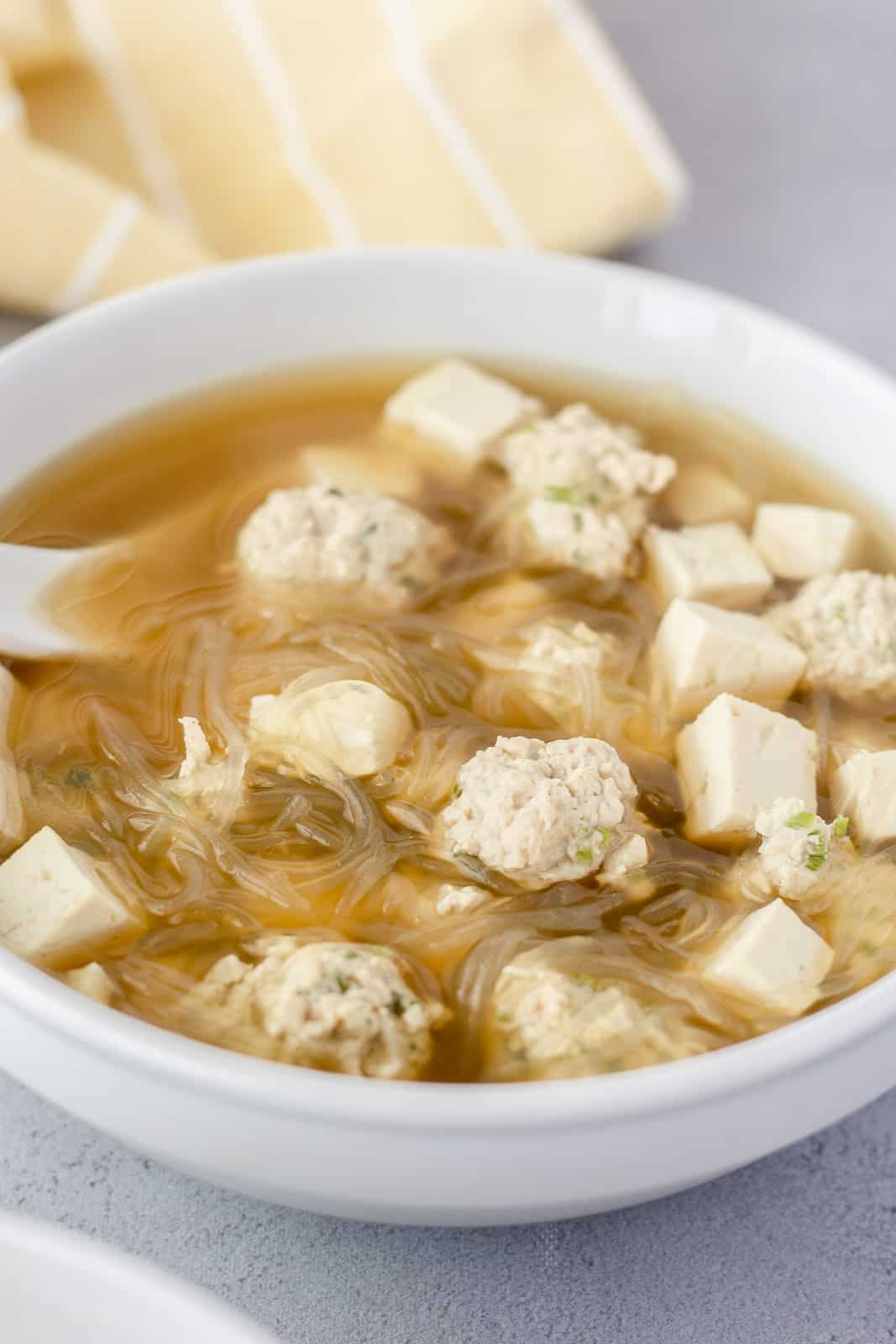 Thai glass noodle soup in a white bowl with meatballs and tofu.