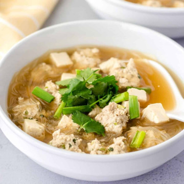 Soup in a white bowl with clean noodles, meatballs, and tofu.