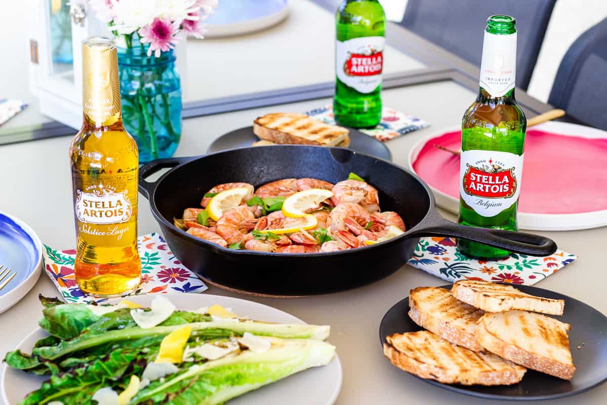 Table setup with plates, grilled romaine, Stella Artois Beers and skillet with shrimp.