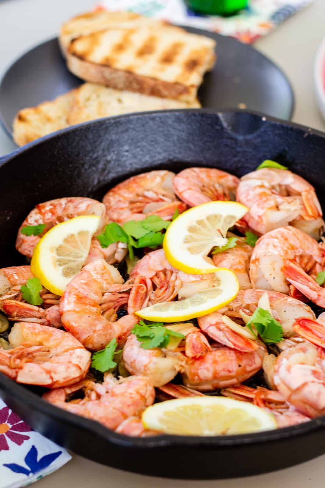 Shrimp in a cast iron skillet garnished with lemon slices and cilantro leaves.