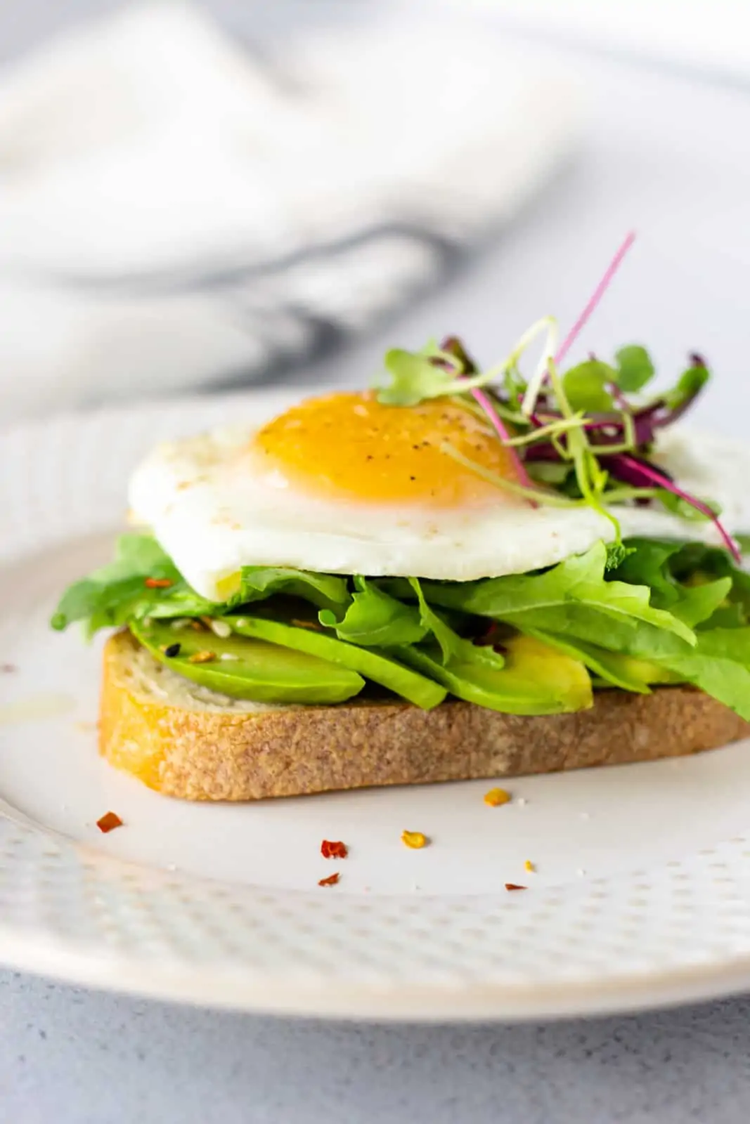 Avocado toast topped with a sunny side up egg and micro greens.