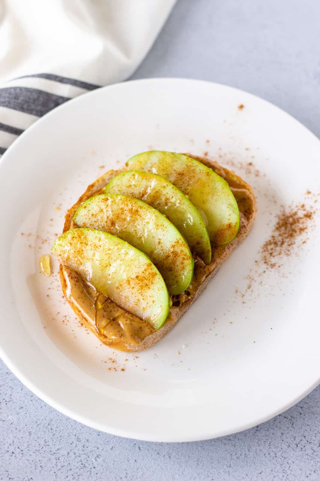 Toast with peanut butter, sliced apples, cinnamon, and honey on a white plate.