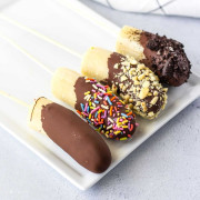 4 dipped bananas with different toppings on a white plate.