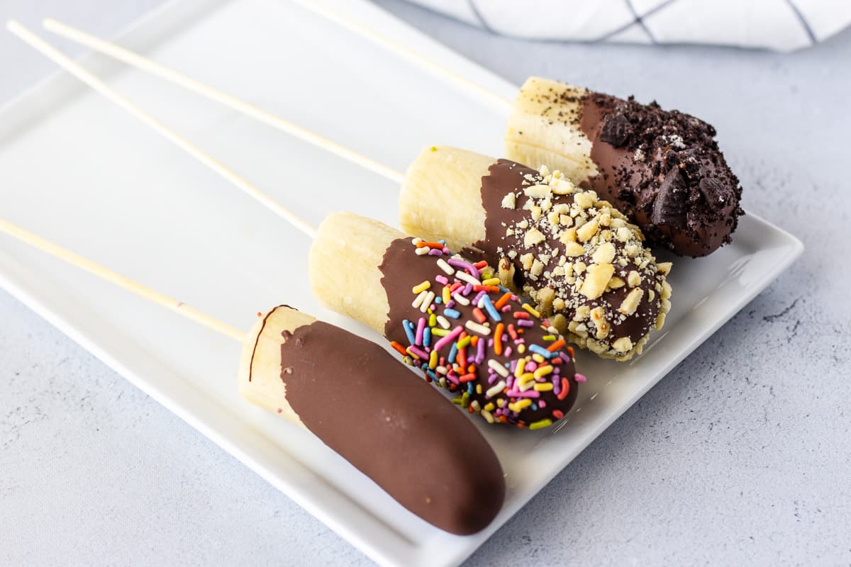 4 Dipped chocolate bananas on a white plate.