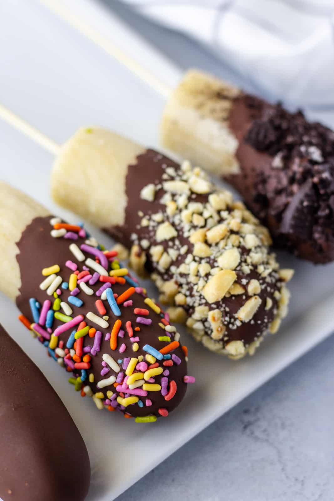 Up close view of dipped bananas with sprinkles and crushed peanuts.
