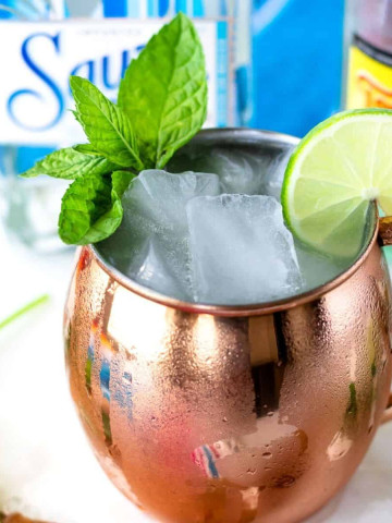 Mexican mule cocktail in a copper mug with condensation on the side and a mint and lime slice garnish.