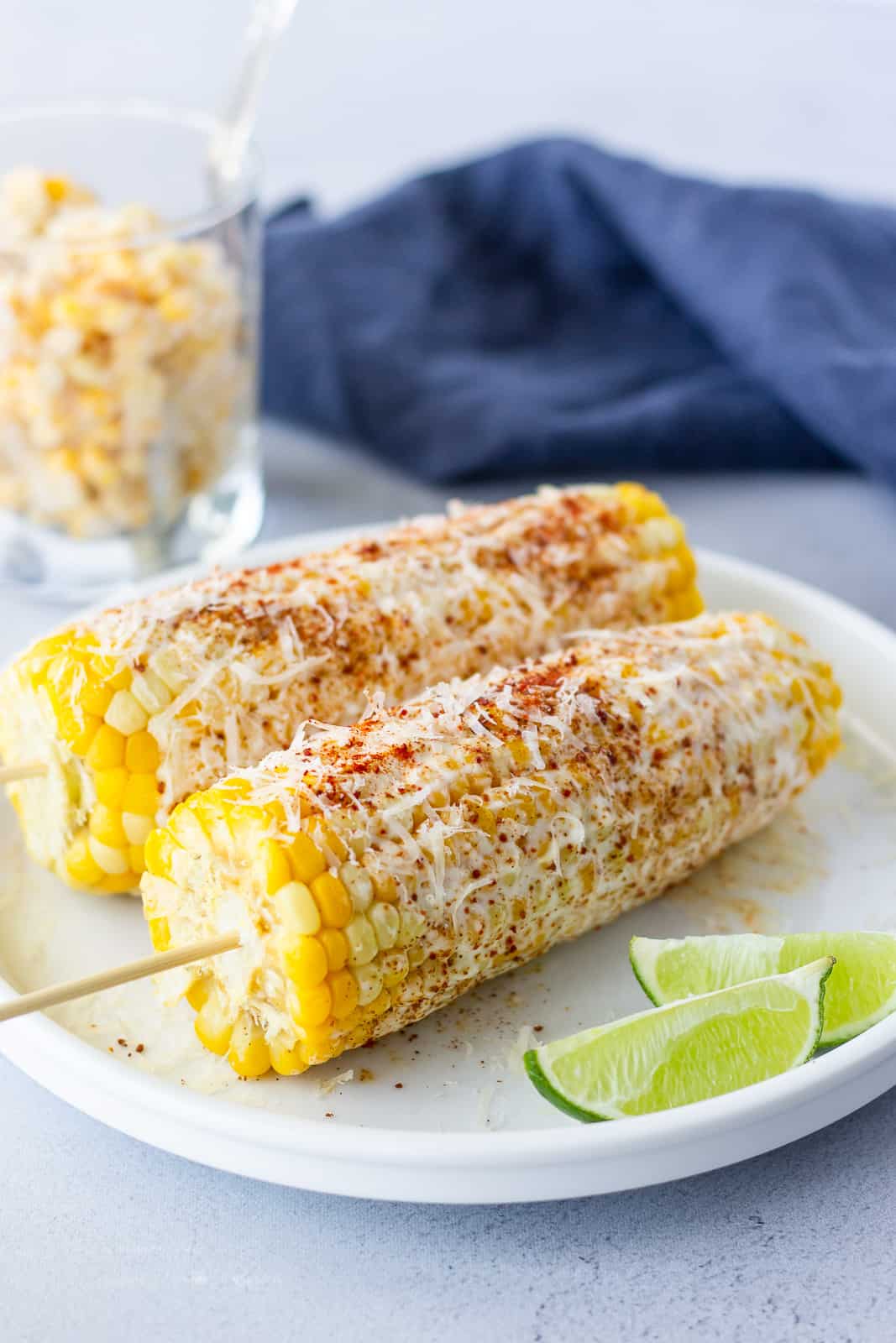 2 ears of corn on a white plate with a glass on the side of shaved corn.