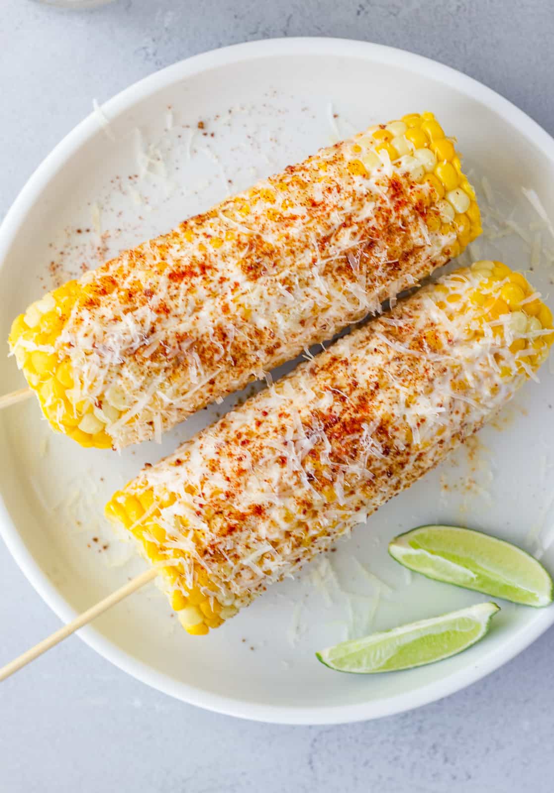 Overhead view of 2 Ears or corn on a white plate with 2 lime wedges on the side.