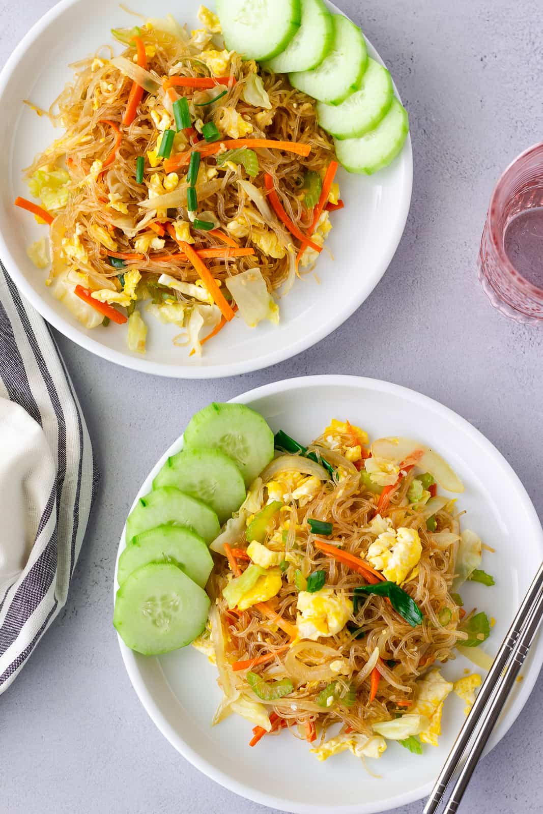 Overhead view of 2 plates with noodles and sliced cucumbers on the side.