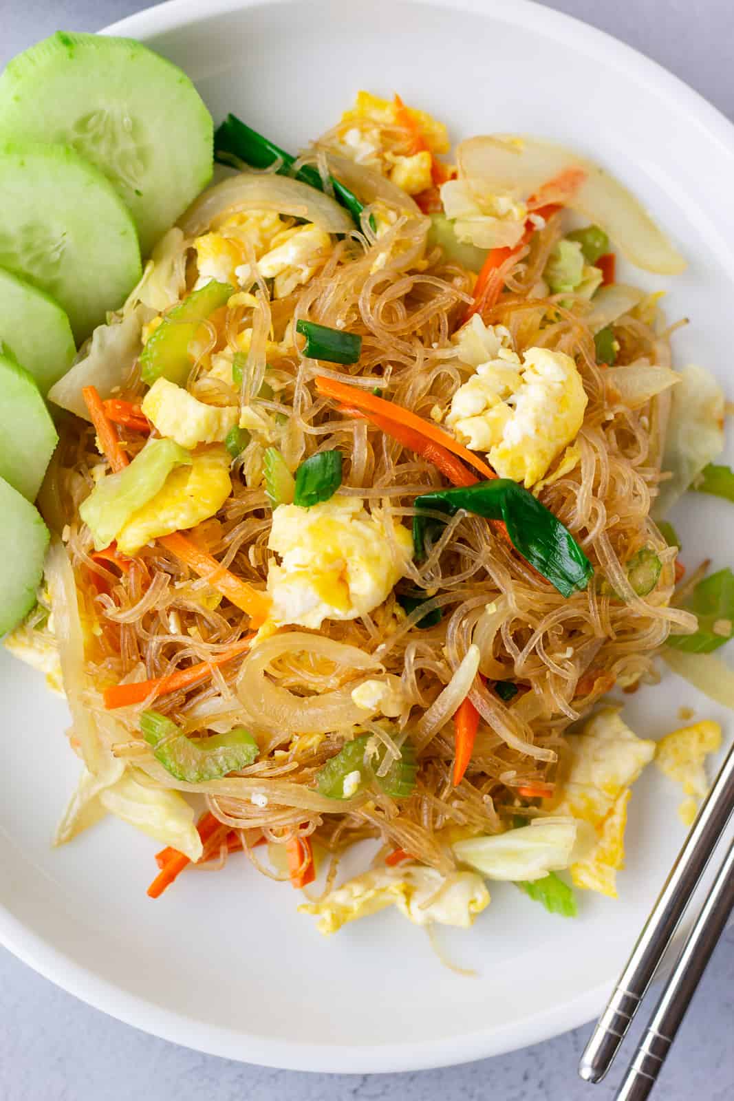 Overhead view of glass noodle dish on a white plate with sliced cucumbers on the side.