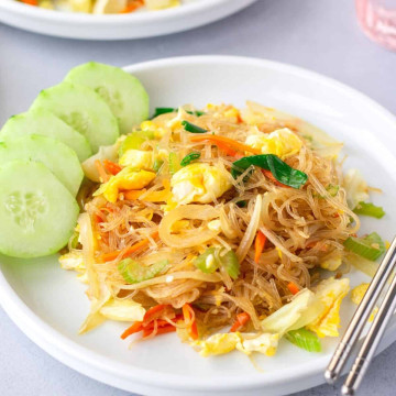 Featured image of pad woo sen on a white plate with sliced cucumbers on the side.