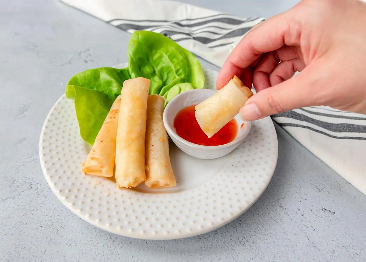 Hand holding a cheese roll being dipped into sweet chili sauce.