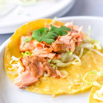 up close view of salmon on yellow corn tortilla with shredded cabbage, chipotle sauce, and cilantro.