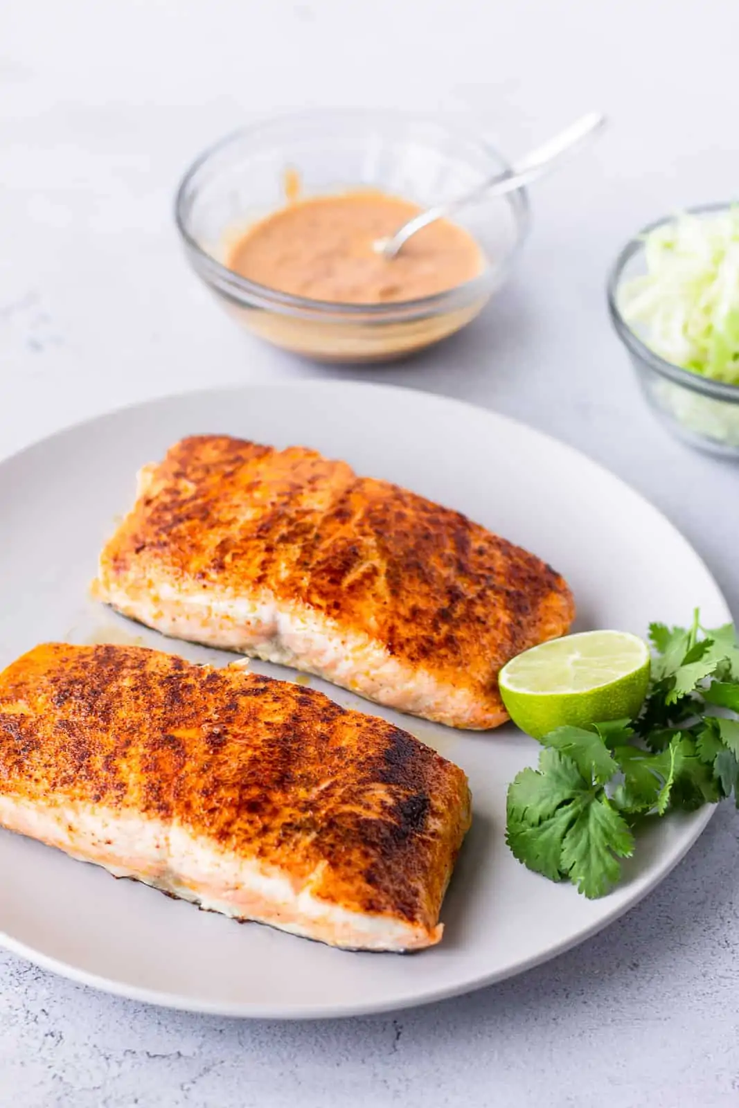 2 cooked salmon fillets garnished with lime and cilantro on the side.