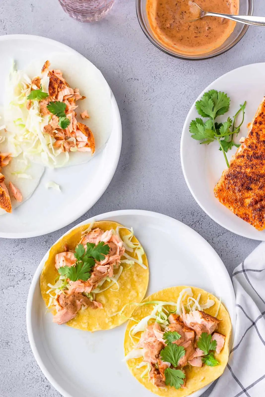 Overhead view of 2 salmon tacos on jicama wraps and 2 salmon tacos on yellow corn tortillas with a side of chipotle sauce.