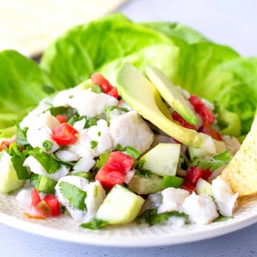 Fish ceviche on a plate with lettuce leaves and topped with sliced avocado.