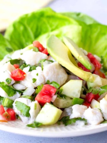 Fish ceviche on a plate with lettuce leaves and topped with sliced avocado.