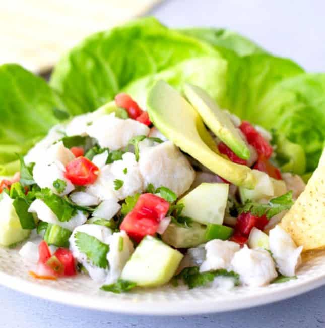 Fish ceviche on a plate with lettuce leaves and topped with sliced avocado.